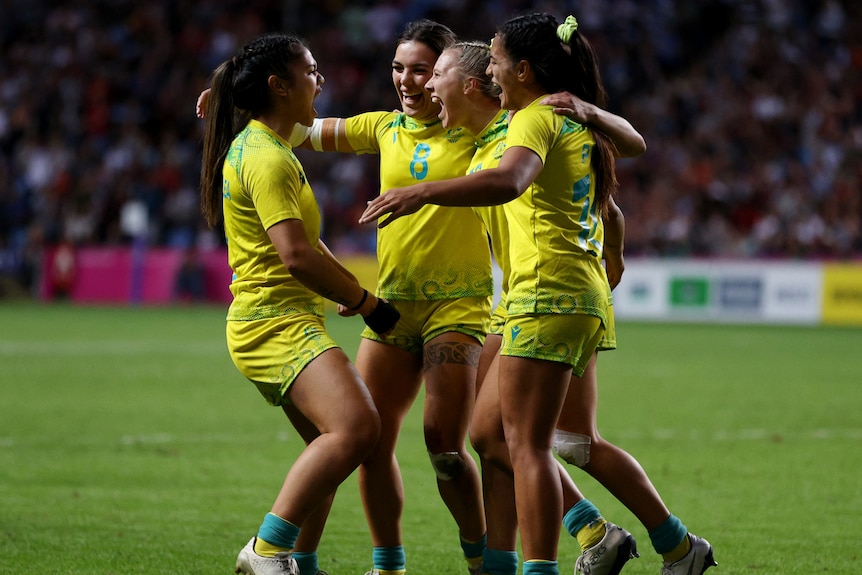 Four Australian women's rugby sevens players have a group hug in mid-pitch after winning Commonwealth Games gold.