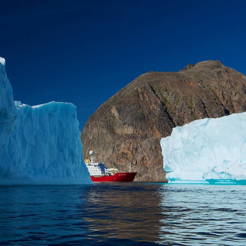A red and white ship floats between icebergs