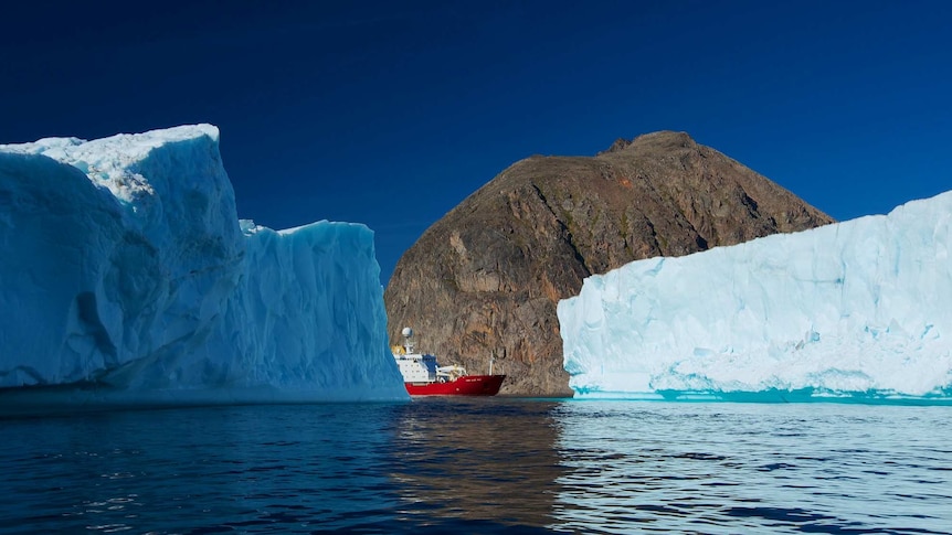 A red and white ship floats between icebergs