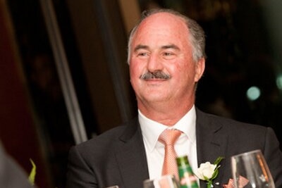 A man in suit and tie sits at a table with glasses of wine and bottles of beer on it.