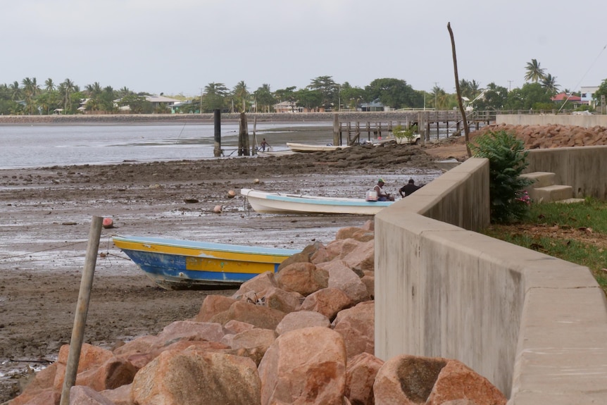 Low tide on a remote Torres Strait island, mudflats and small fishing boats in foreground, with a village beyond