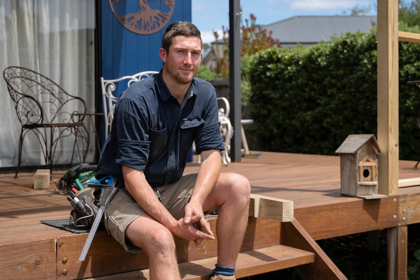 A carpenter sits on the wooden back deck of a house