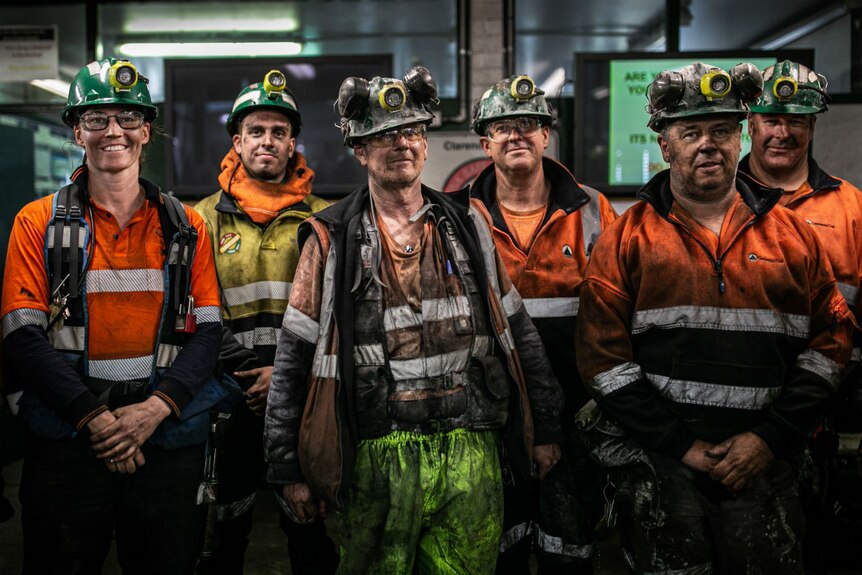 A group of men and one woman wearing high-vis clothing and helmets and covered in soot.