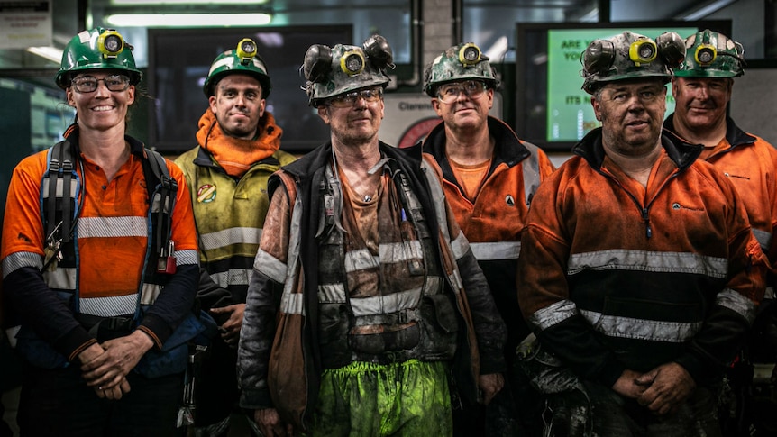 A group of men and one woman wearing high-vis clothing and helmets and covered in soot.