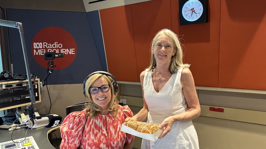 Two women smiing in radio studio holding hot cross buns 