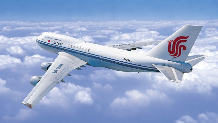 View of an Air China branded plane from above, as it flies above a layer of clouds.