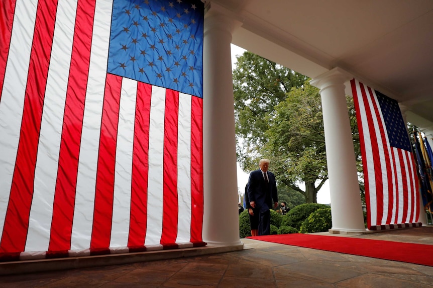 U.S President Donald Trump walks past two large American flags