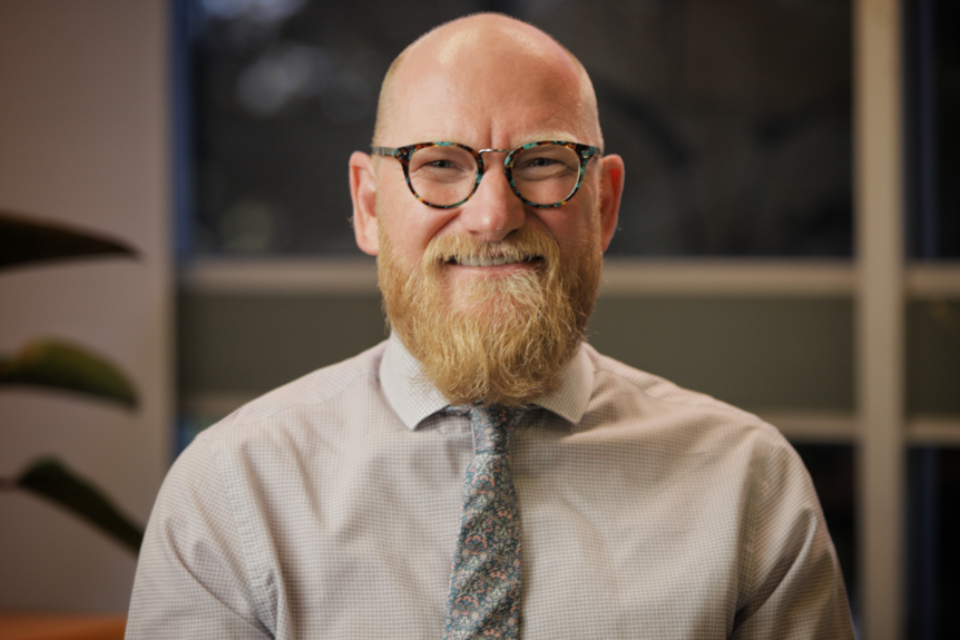 Man with a beard, wearing glasses, a business shirt and tie.