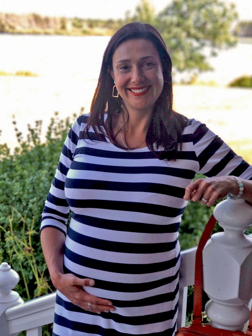 A pregnant woman leans on a bannister in front of a garden.