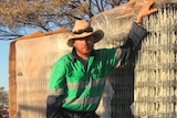 A man wearing an akubra stands by fencing material.