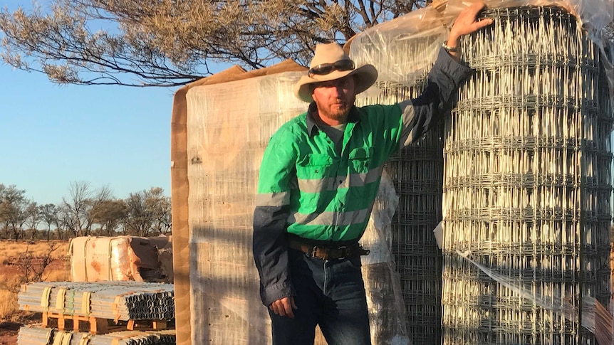 A man wearing an akubra stands by fencing material.