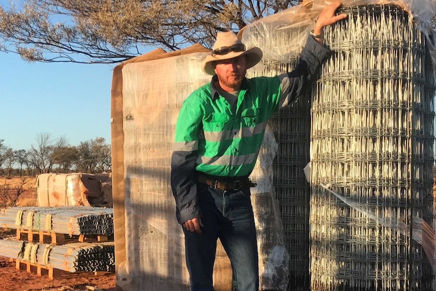 A man wearing an akubra stands by fencing material.