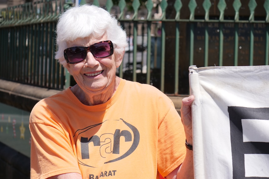 A woman wearing a bright orange t-shirt and sunglasses smiles.