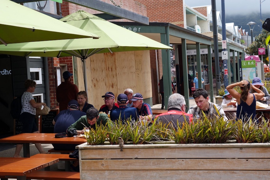 People sit at tables outside on a footpath.