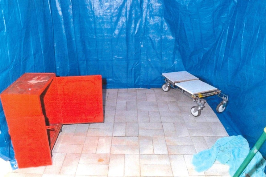 A photo of a room with the walls covered in blue tarpaulin, with a wood chest on the left and trolley on the right.