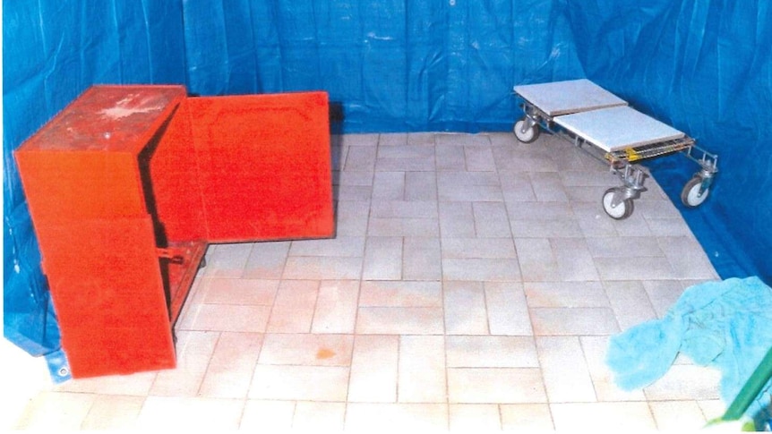 A photo of a room with the walls covered in blue tarpaulin, with a wood chest on the left and trolley on the right.