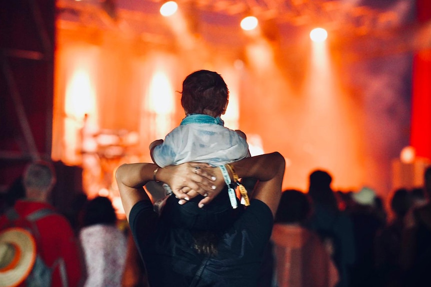 A child sits on a man's shoulders and watches a band on stage at Bluesfest 2022