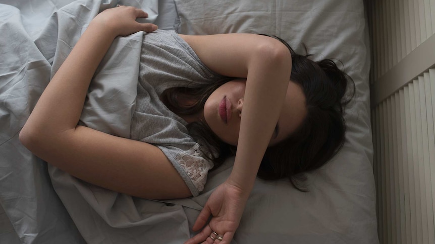 A woman lies in bed with a hand over her face