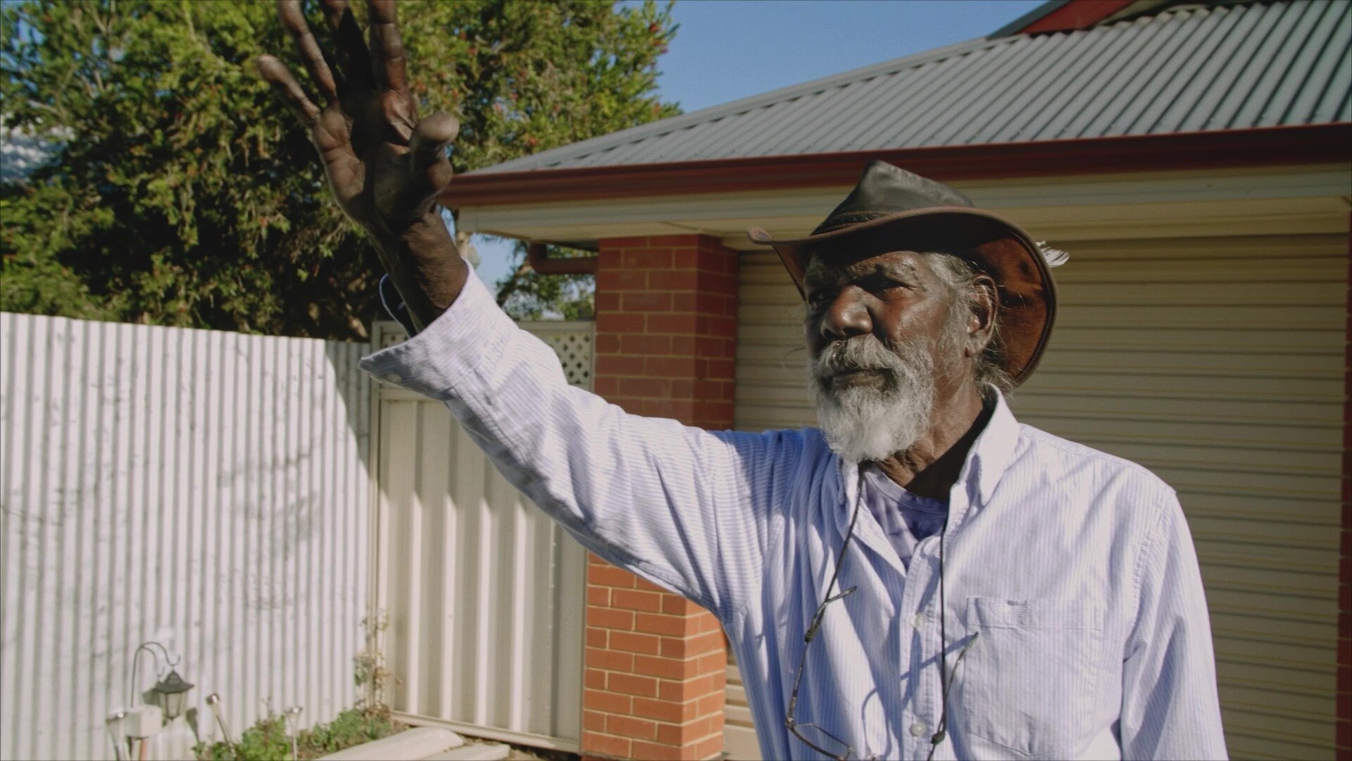 A man wearing a hat, waving to someone off-screen.