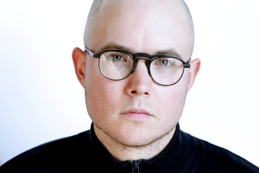 A close up photo of a bald white man wearing glasses and a dark shirt.
