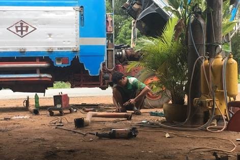 A man squats on the ground as he undertakes mechanical work at a repair shop.
