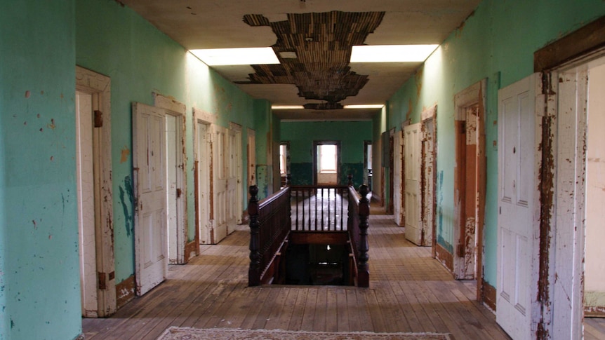Picture of a hallway with several doors on either side, looking run down with chipped paint