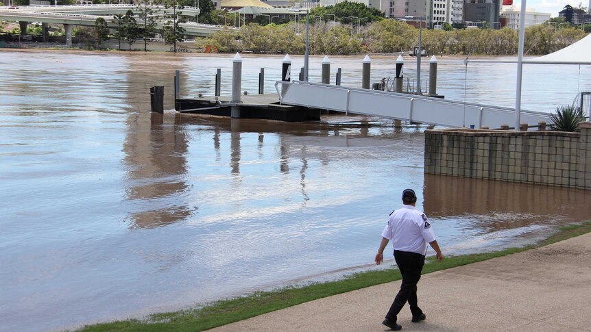 A security guard walks beside the Brisbane River as a pontoon rides out today's flood peak