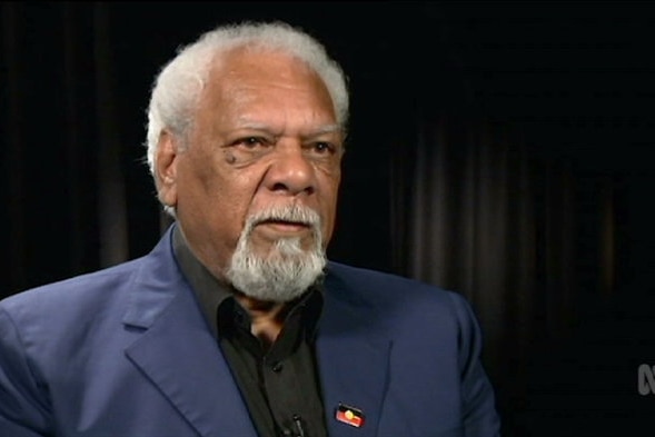 An Aboriginal man with grey hair sitting for an interview while wearing a navy blue suit.
