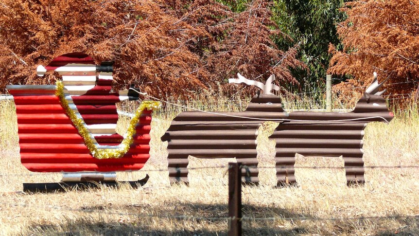 a corrugated iron cut out of Santa on a sleigh with reindeers in a dry grass paddock.