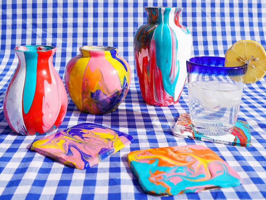 Colourfully painted vases and coasters sit on a blue check tablecloth.