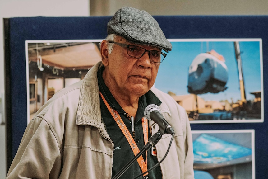 An elderly Aboriginal man wearing a cap speaking into a microphone.  