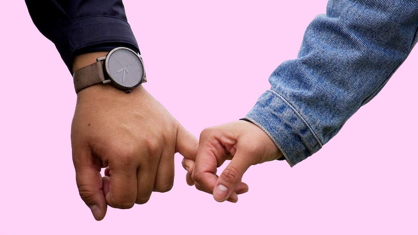 A couple gently holding hands against a pink background for a story about breaking up when the timing isn't right.