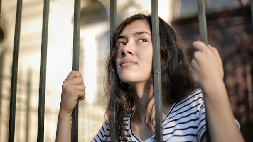 A woman stares into the distance as she holds on to vertical bars in front of her.