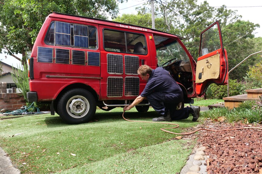 A man kneels down to plug in a power cable into the bottom of the van