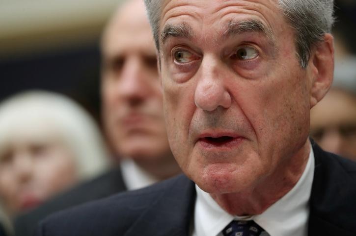 Robert Mueller looks to the left with his mouth open and his eyes wide. He wears a suit and people are seen behind him.