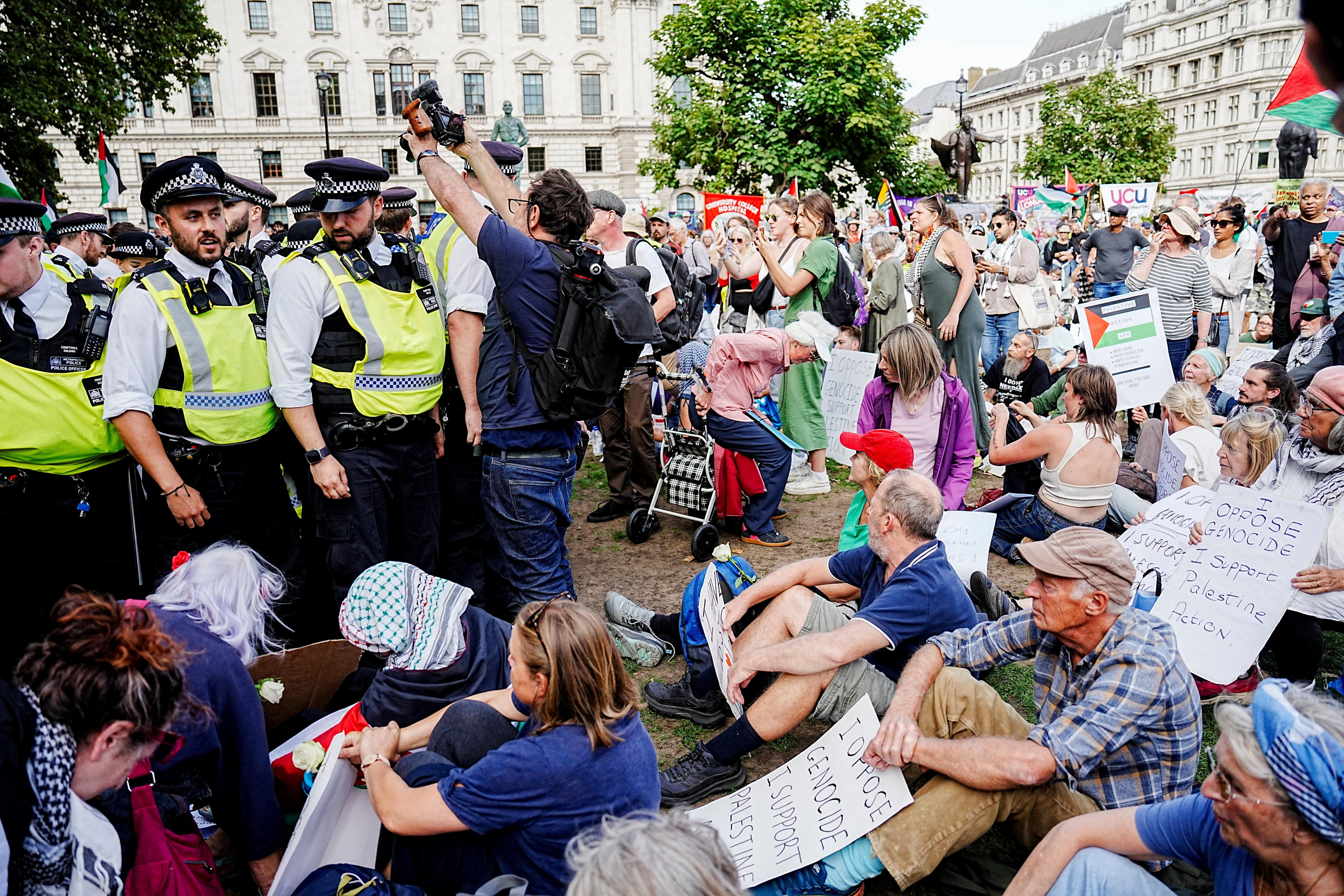 Police officers standing in high-vis jackets as people sit on the grass around them.