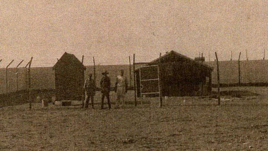 Sepia photo of three men standing behind a fence in a yard at the hospital grounds