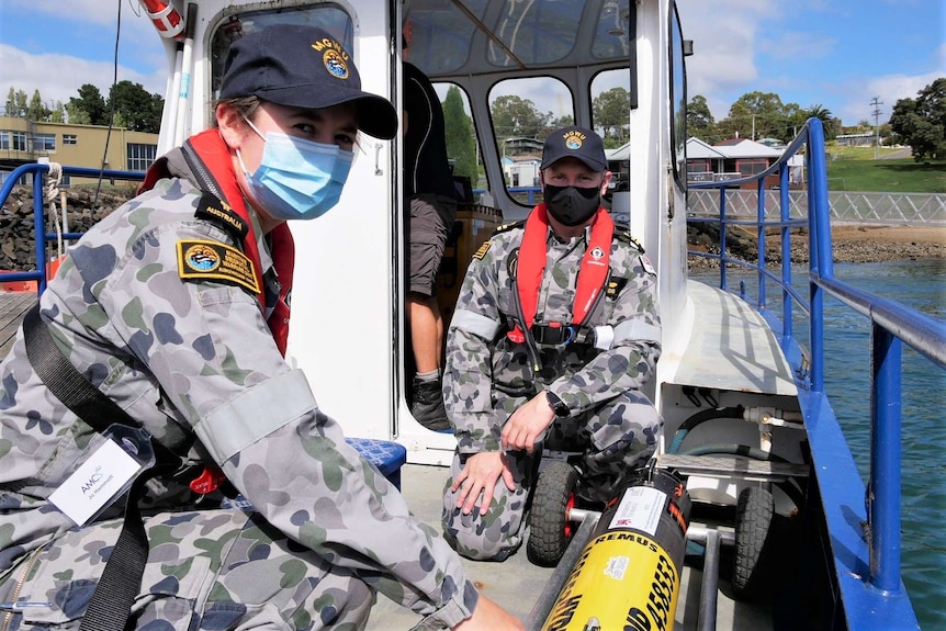 Two Navy personnel sit with an AUV on board a boat.