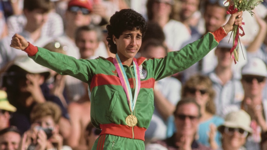 Nawal El Moutawakel stands on the winning podium with her arms in the air at the Los Angeles 1984 Olympics.