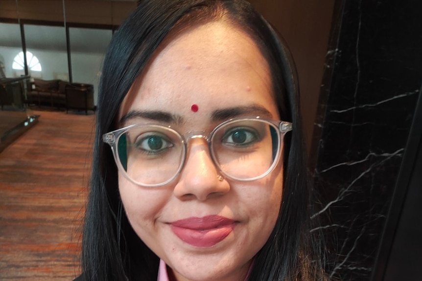 A young woman wearing with long black hair wearing glasses and a black blazer.