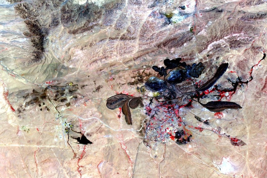 An aerial photo shows a sand-coloured landscape with plenty of black splotches due to rare earth mining.