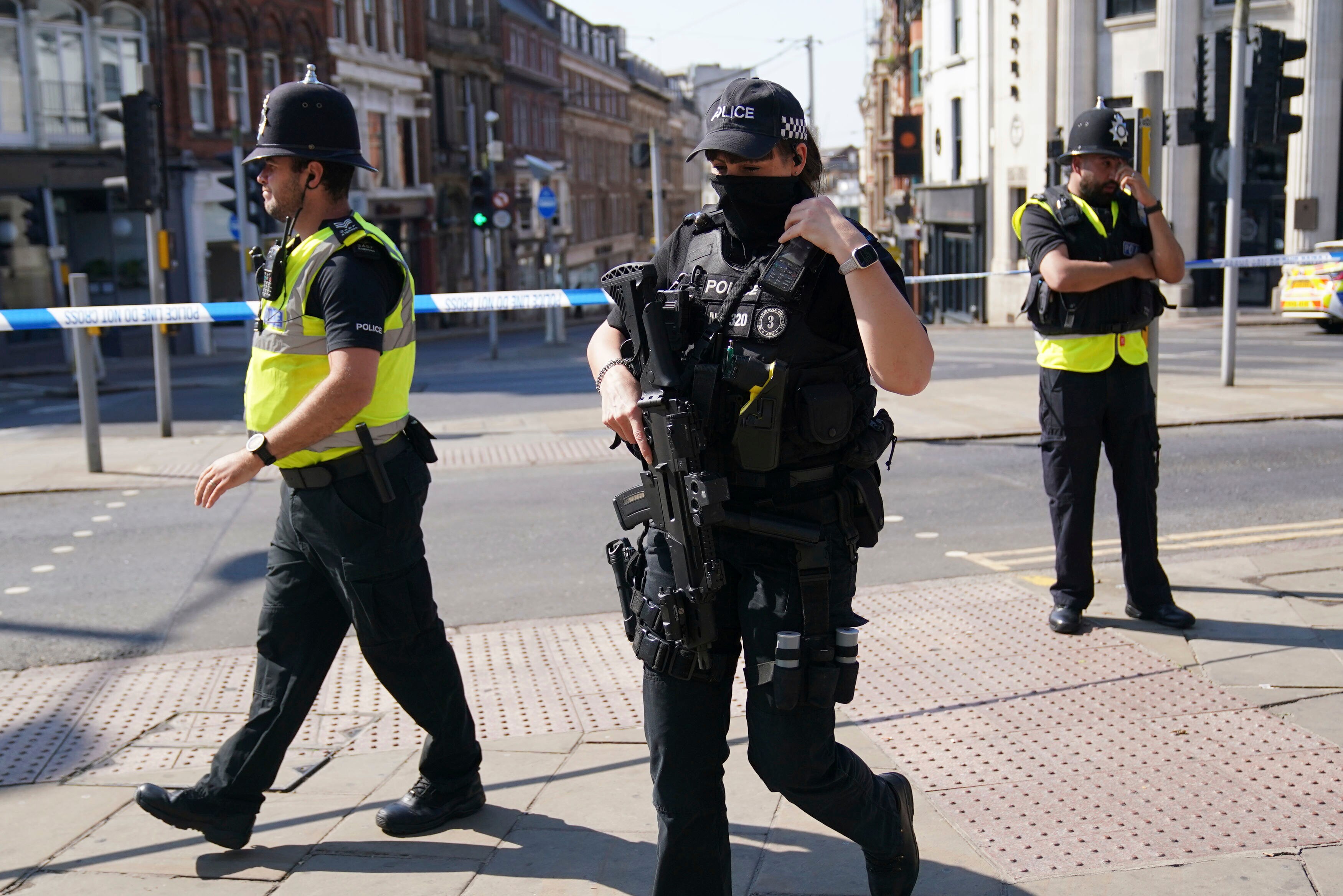 A police officer in a hi-vis vest walks with a police officer head to toe in protective gear holding a gun.