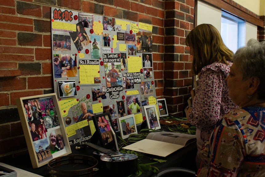 Two woman look at a poster collage with photos of Chris Collie and messages to him.