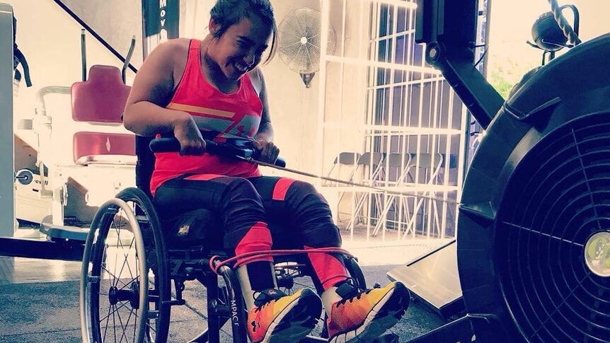 A young woman sits in a wheelchair with her feet on a gym rower, pulling the rope back.