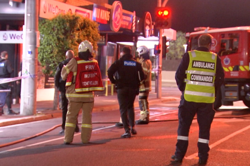 A firefighter wearing a helmet, a police officer and an ambulance commander stand in the street near a fire truck.