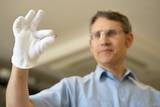 Professor Paul Dastoor holding a tiny saliva glucose biosensor strip between his thumb and forefinger