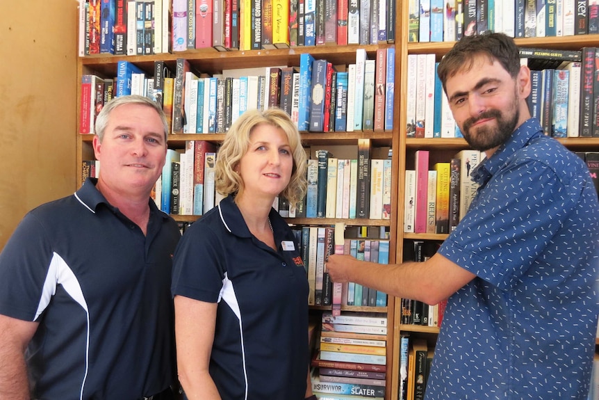 Grant Searles, Jenny Reeve and Ben Kelly stand in front of a massive bookshelf.  Ben reaches for a book.