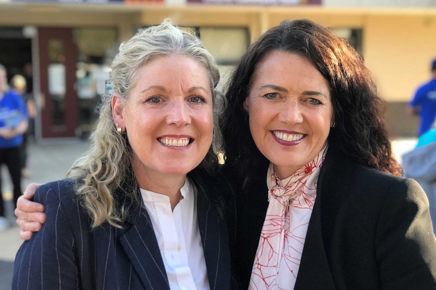 Libby Coker and her sister Janet stand with their arms about each other, outside a polling booth.