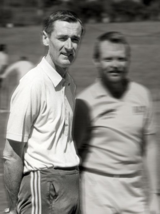 Black and white image of three men on a sports field chatting, 2 out-of-focus, 1 in-focus