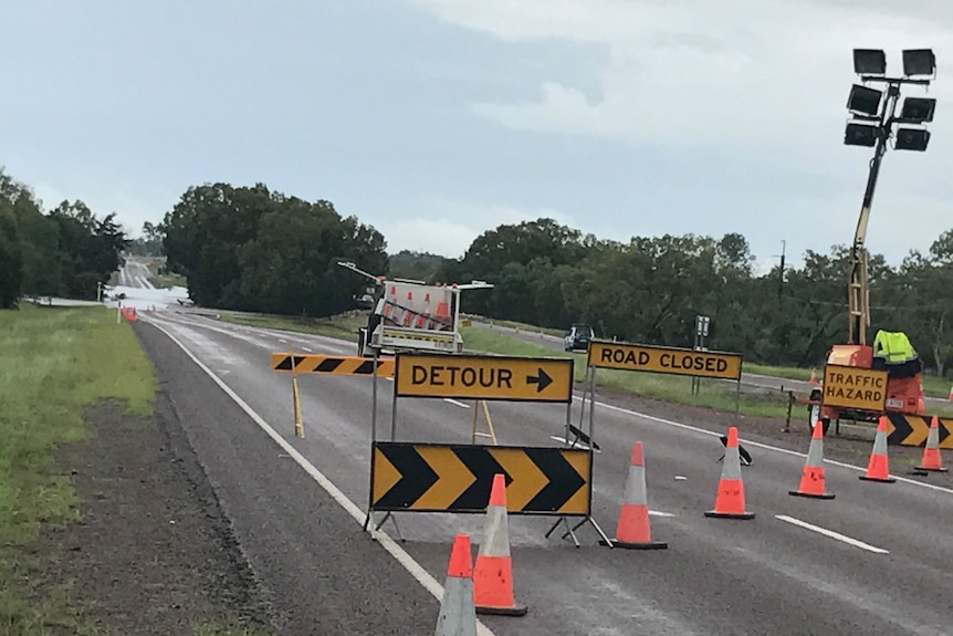 Road closure signs across a road with water over the road.